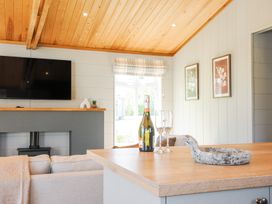 A living room with a mounted television above a fireplace and a kitchen counter with a bottle and two glasses at 17 Meadow Retreat in Dobwalls