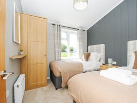 A bedroom with two single beds a wooden wardrobe and a window with plaid curtains at 17 Meadow Retreat in Dobwalls