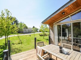 A wooden patio with a table and chairs next to a house with glass doors and a grassy yard with trees at 17 Meadow Retreat in Dobwalls