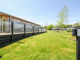 A grassy lawn with small trees next to wooden buildings with glass railings at 17 Meadow Retreat in Dobwalls