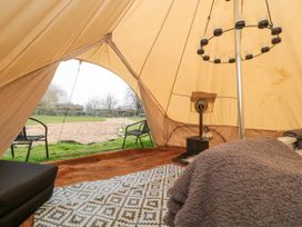 The interior of a bell tent with a wood stove a patterned rug chairs outside and a candle chandelier at Bell tent 3 in Camerton near Timsbury