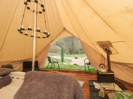 The interior of a bell tent with a bed covered in blankets a metal candle holder two chairs outside on grass a wood stove with a kettle and fire starter supplies at Bell tent 3 in Camerton near Timsbury