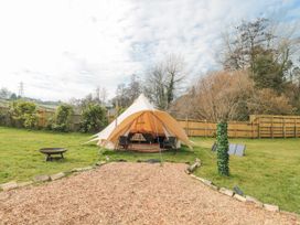 An outdoor area with a bell tent on grass surrounded by a wooden fence and trees at Bell tent 3 Camerton near Timsbury