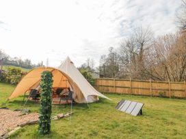 A bell tent with chairs and a rug inside set up on grass with a wooden fence and trees in the background at Bell tent 3 in Camerton near Timsbury
