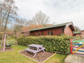 A wooden cabin with a hedge a purple picnic table and a swing set in a grassy yard at Bell tent 3 in Camerton near Timsbury