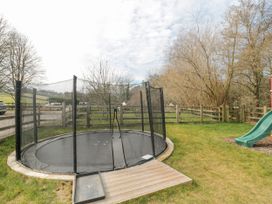 An outdoor fenced grassy area with a round trampoline and a green slide at Bell tent 3 in Camerton near Timsbury