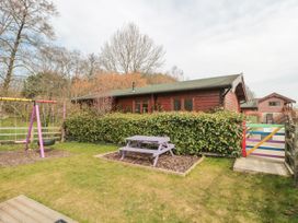 An outdoor area with a wooden picnic table, a swing set, and a wooden cabin behind bushes at Bell tent 3 in Camerton near Timsbury