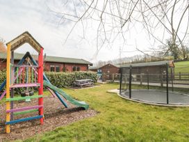 A playground with a slide swing and trampoline next to wooden buildings at Bell tent 3 in Camerton near Timsbury