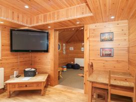 A wooden room with a wall-mounted TV table with electronics and a dining table with chairs at Bell tent 3 Camerton near Timsbury