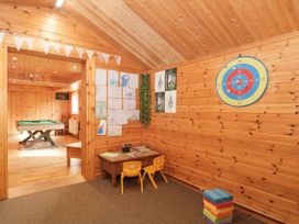 A children's playroom with wooden walls featuring drawings on one wall a small table with two chairs and a dartboard on another wall with a pool table in an adjoining room at Bell tent 3 Camerton near Timsbury
