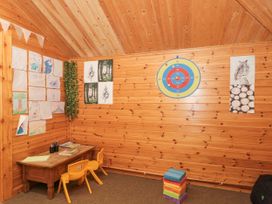 A wooden room with a small table and two yellow chairs children's drawings on the walls a dartboard and a stack of colored blocks at Bell tent 3 in Camerton near Timsbury