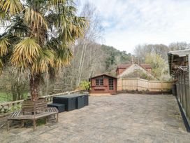 A patio with a wooden bench around a palm tree a table with chairs a wooden shed and a wooden fence at Bell tent 3 in Camerton near Timsbury
