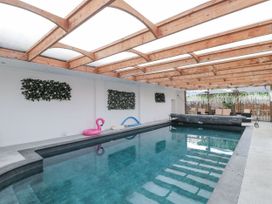An indoor swimming pool with wooden beams on the ceiling a pink flamingo float on the side and seating area at Bell tent 3 Camerton near Timsbury