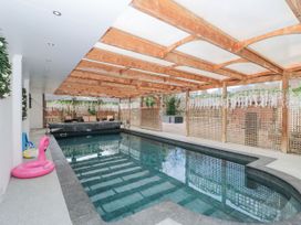 An indoor pool with a wooden roof structure and hanging plants surrounded by seating at Bell tent 3 in Camerton near Timsbury