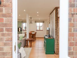 View through an open door of a living and dining area with sofas, a wooden dining table, green cabinet with a television and exposed wooden beams at The Round House in Wardington near Chacombe
