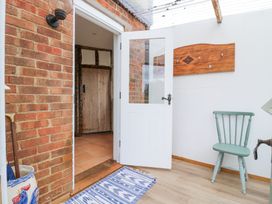 A hallway with a white door open to a tiled room a green chair a wooden coat rack on the wall and a blue patterned rug on the floor at The Round House in Wardington near Chacombe