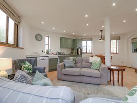 An open living area with sofas and cushions a kitchen with green cabinets and appliances and a wooden dining table at The Round House in Wardington near Chacombe