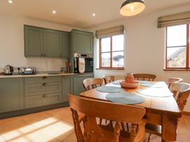 A kitchen with a wooden dining table and chairs next to green cabinets and two windows at The Round House in Wardington near Chacombe
