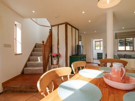A dining area with wooden chairs and a table with placemats and a jug set next to stairs and a green cabinet with a TV at The Round House in Wardington near Chacombe