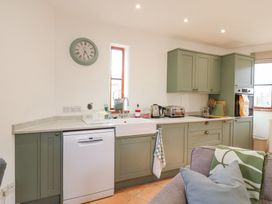 A kitchen with green cabinets a white dishwasher a farmhouse sink and a wall clock at The Round House in Wardington near Chacombe