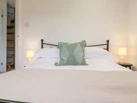 A bedroom with a metal bed frame white bedding a green cushion two bedside tables with lamps and a wooden spiral staircase in the background at The Round House in Wardington near Chacombe