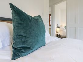 A large green cushion on a bed with white bedding in a bedroom with a view into another bedroom at The Round House in Wardington near Chacombe