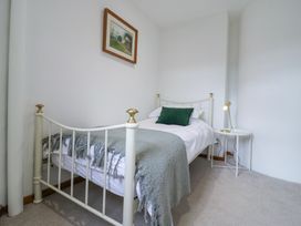 A small bedroom with a single metal bed frame with white and green bedding and a gray throw blanket with a round side table and lamp at The Round House in Wardington near Chacombe