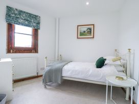 A bedroom with a single bed a bedside table with a lamp a window with floral curtains and a painting on the wall at The Round House in Wardington near Chacombe