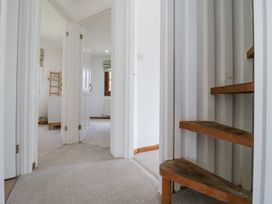 A hallway with carpeted floor leading to rooms with open doors and wooden stairs on the right at The Round House in Wardington near Chacombe