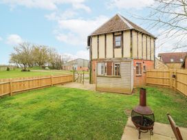 A small fenced backyard with grass and a chiminea next to a two-story house with a tiled roof at The Round House in Wardington near Chacombe