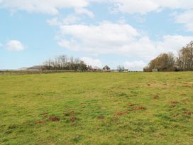 A grassy field with scattered molehills and buildings in the distance at The Round House in Wardington near Chacombe