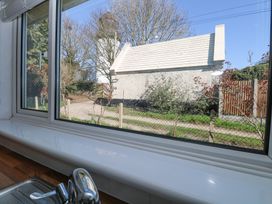 A kitchen window with a sink and faucet showing an outdoor view of a white building and trees at Lighthouse View in Winterton-On-Sea
