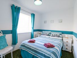 A bedroom with a double bed striped bedding teal curtains white bedside tables and a white chair at Lighthouse View in Winterton-On-Sea