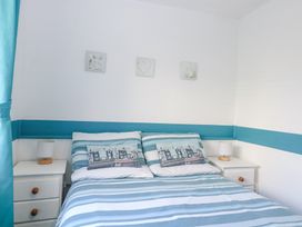 A bedroom with a double bed with striped blue and white bedding and two white nightstands with lamps at Lighthouse View Winterton-On-Sea