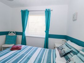 A bedroom with a bed with striped bedding a window with teal curtains and a chair with a teal cushion at Lighthouse View in Winterton-On-Sea