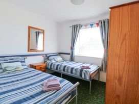 A bedroom with two single beds a wooden nightstand a wall mirror striped curtains and a wooden wardrobe at Lighthouse View in Winterton-On-Sea