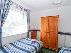 A bedroom with two single beds a wooden wardrobe and a window with striped curtains at Lighthouse View in Winterton-On-Sea