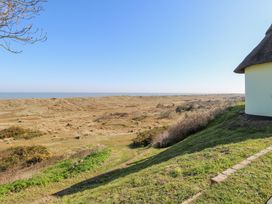 A landscape view of grassy dunes and shrubs by the sea with part of a thatched roof building on the right at Lighthouse View in Winterton-On-Sea