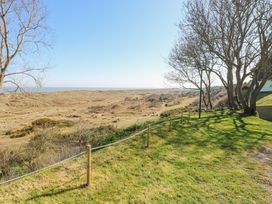 A grassy area with a rope fence near a field with bushes and trees at Lighthouse View in Winterton-On-Sea