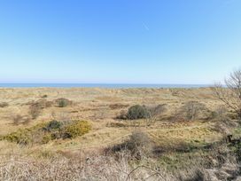 A landscape with dry grass and scattered bushes with the ocean in the distance at Lighthouse View in Winterton-On-Sea