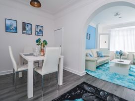 A dining area with white chairs and table next to a living room with cream sofas and a blue rug at Anfield Stadium Short Stay and Free Parking in Liverpool