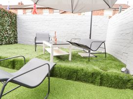 An outdoor seating area with gray chairs a white table and an umbrella on artificial grass at Anfield Stadium Short Stay and Free Parking Liverpool