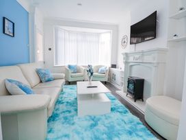 A living room with a white sofa and armchairs blue cushions a blue rug a white coffee table a white fireplace with a black stove and a wall-mounted TV at Anfield Stadium Short Stay and Free Parking in Liverpool