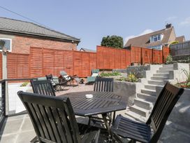 An outdoor patio with a black wooden table and chairs next to concrete steps and garden beds at Colliers Cottage in Cinderford