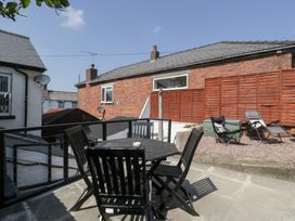 An outdoor patio area with a black table and chairs a gravel section with two lounge chairs and a wooden fence in the background at Colliers Cottage in Cinderford