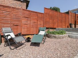 Two lounge chairs with cushions on a pebble ground next to a wooden fence and a small raised garden bed at Colliers Cottage in Cinderford