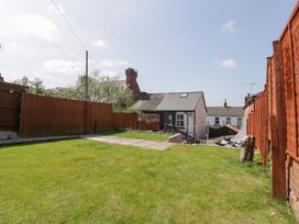A backyard with green grass fenced by wooden panels and houses in the background at Colliers Cottage in Cinderford