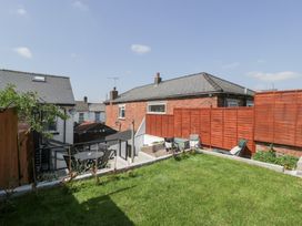 A backyard with a grass lawn a wooden fence outdoor seating and neighboring houses at Colliers Cottage in Cinderford