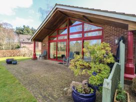 A brick house with large red-framed glass doors and windows on a paved patio with chairs and potted plants at Studio Cottage in Surlingham near Poringland