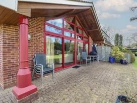 A patio area with stacked chairs a table large red framed windows and potted plants at Studio Cottage in Surlingham near Poringland